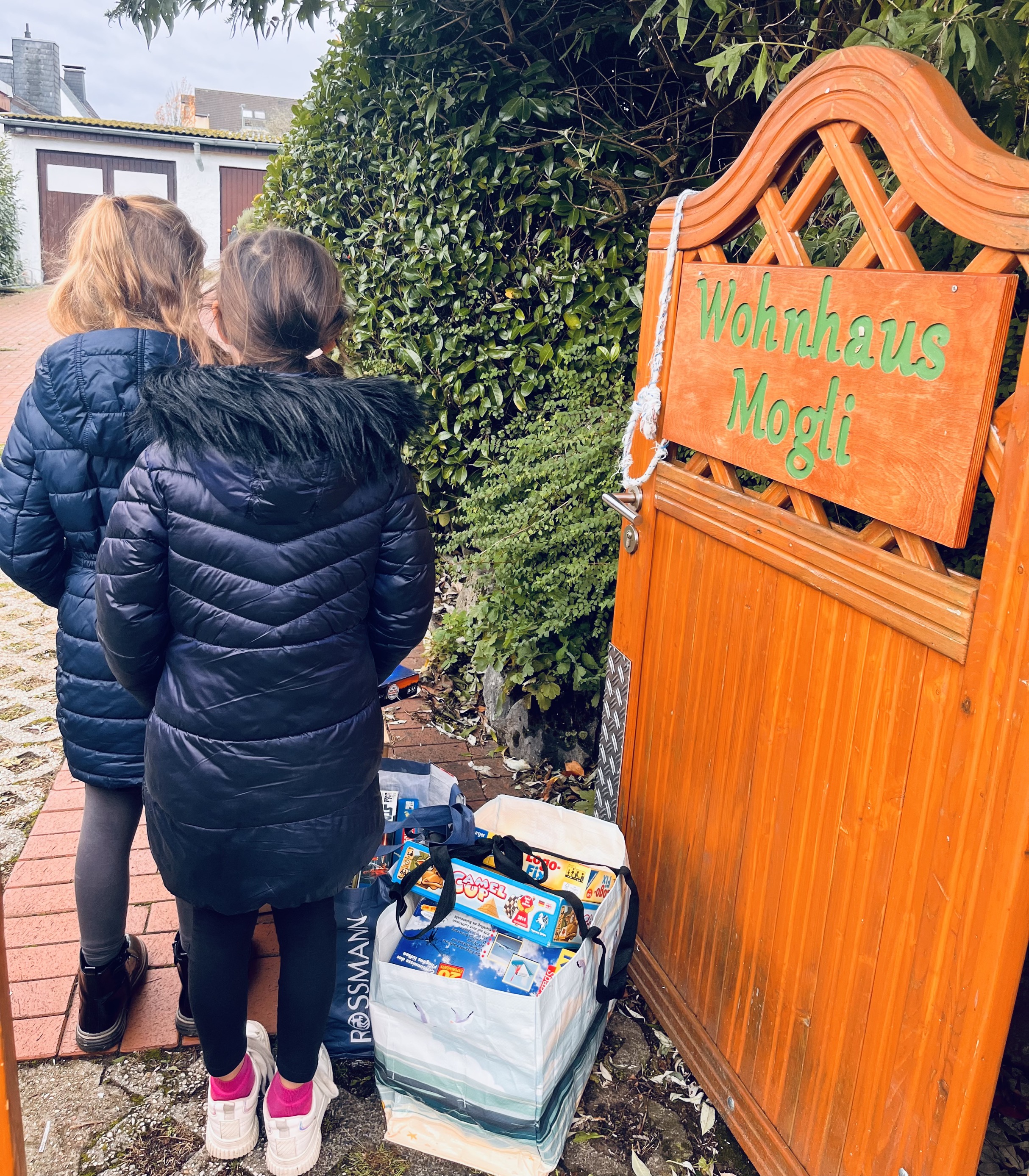 zwei Mädchen stehen am Tor des Kinderheims und übergeben ihre Spielsachenspenden